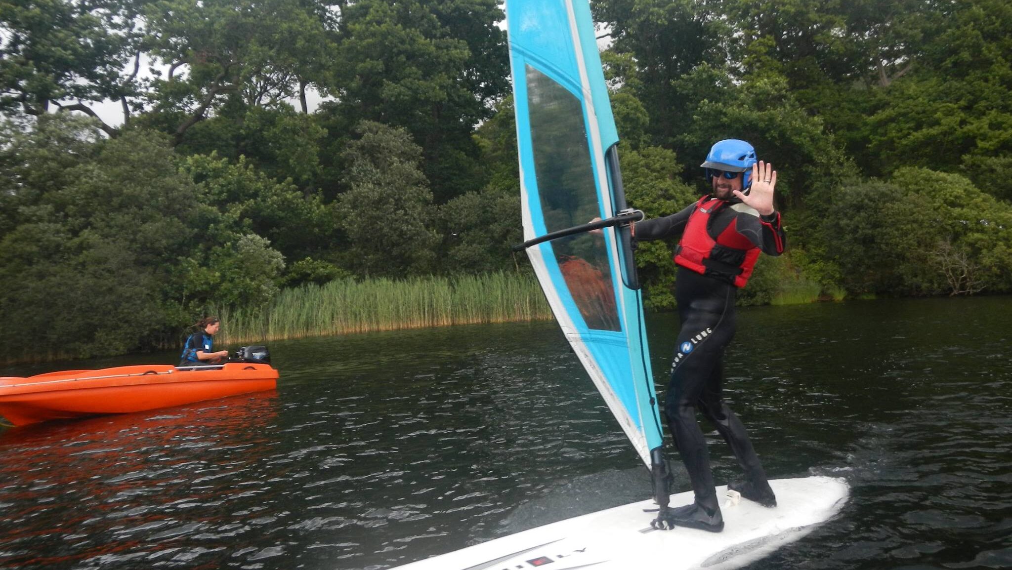 Our Activity Coordinator, James, is waving to the camera on the lake windsurfing.
