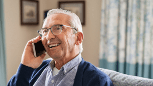 Image of an elderly man holding a smartphone up to his ear smiling.