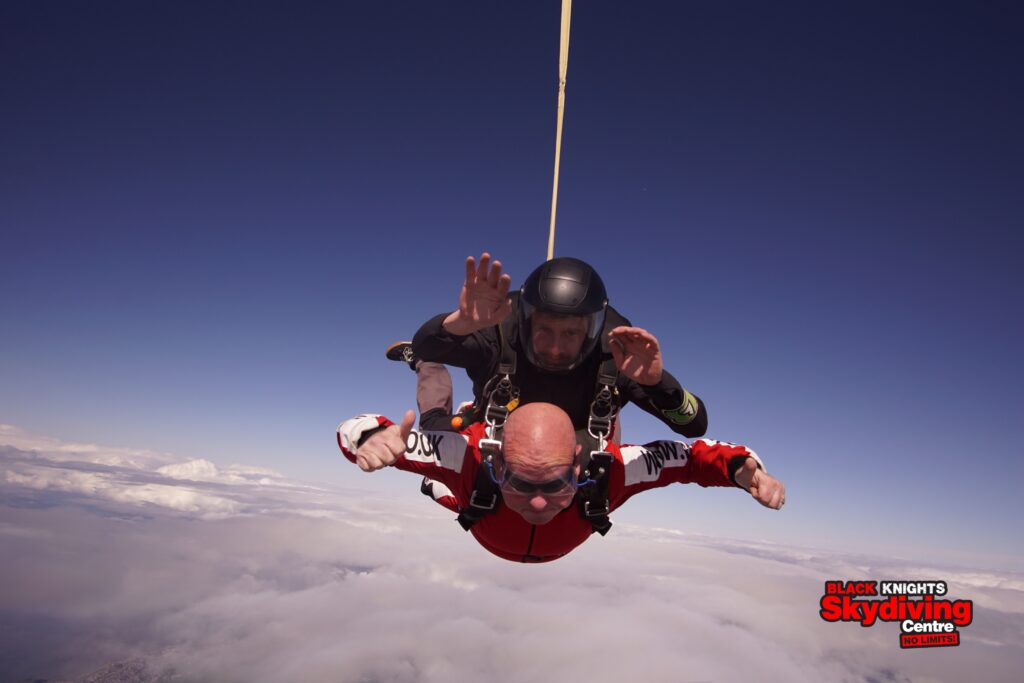 Nigel and instructor in a tandem skydive freefall agains a blue sky and fluffy white clouds below.