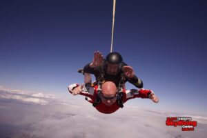 Nigel and instructor in a tandem skydive freefall agains a blue sky and fluffy white clouds below.