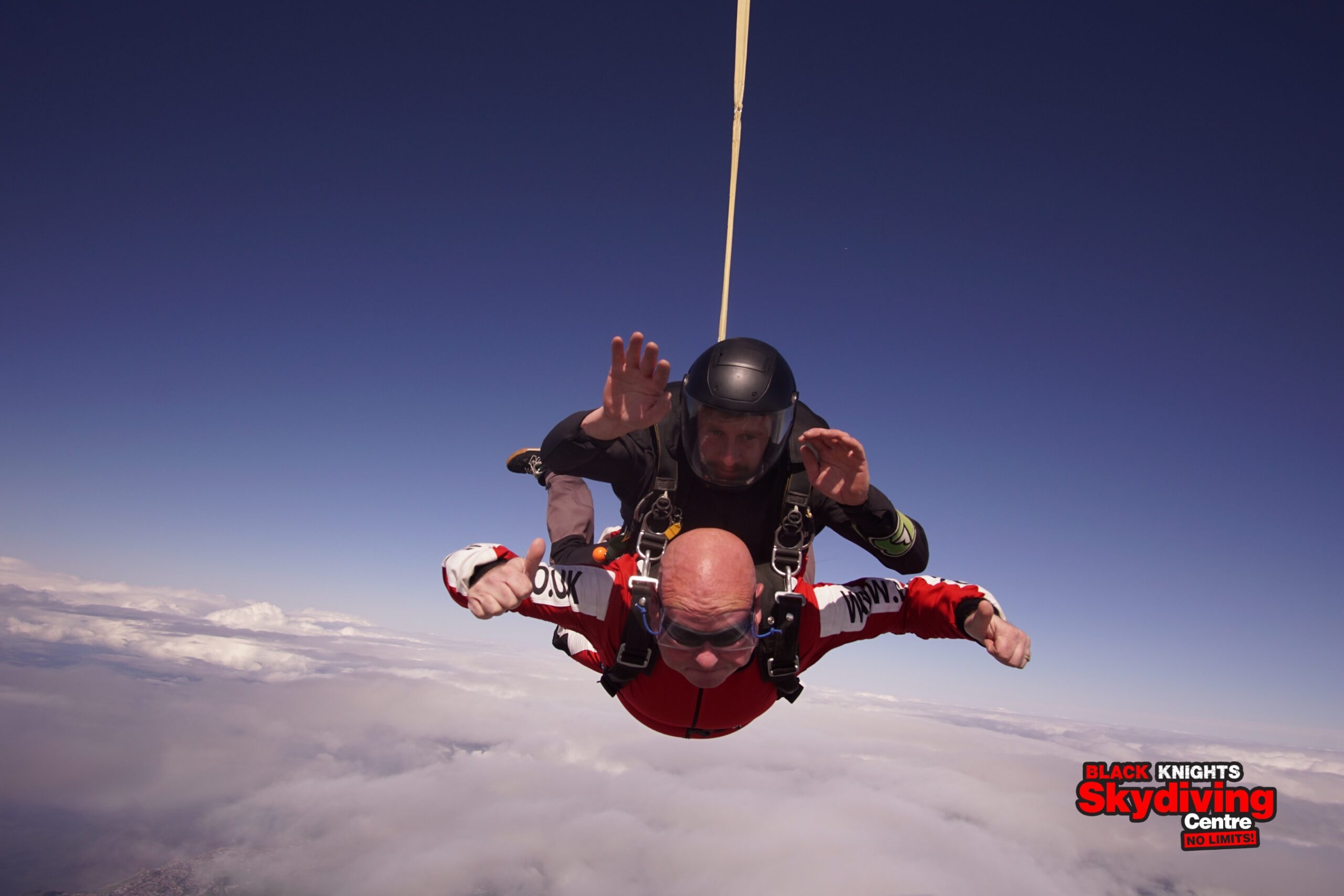 Nigel and instructor in a tandem skydive freefall agains a blue sky and fluffy white clouds below.