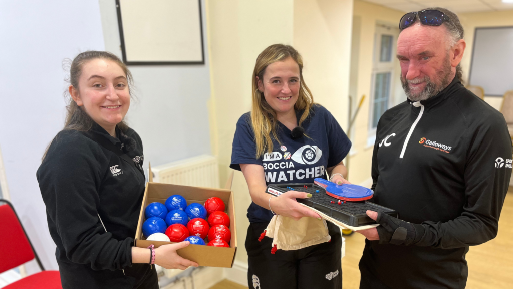 3 people holding Boccia equipment such as a box of blue and red balls, and a tactile handheld table