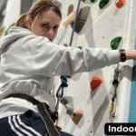 A service user climbing on a wall with a harness around them. The Galloways logo is in the top left corner on top of a orange semi-circle. In the bottom right corner is a caption stating, " indoor climbing".