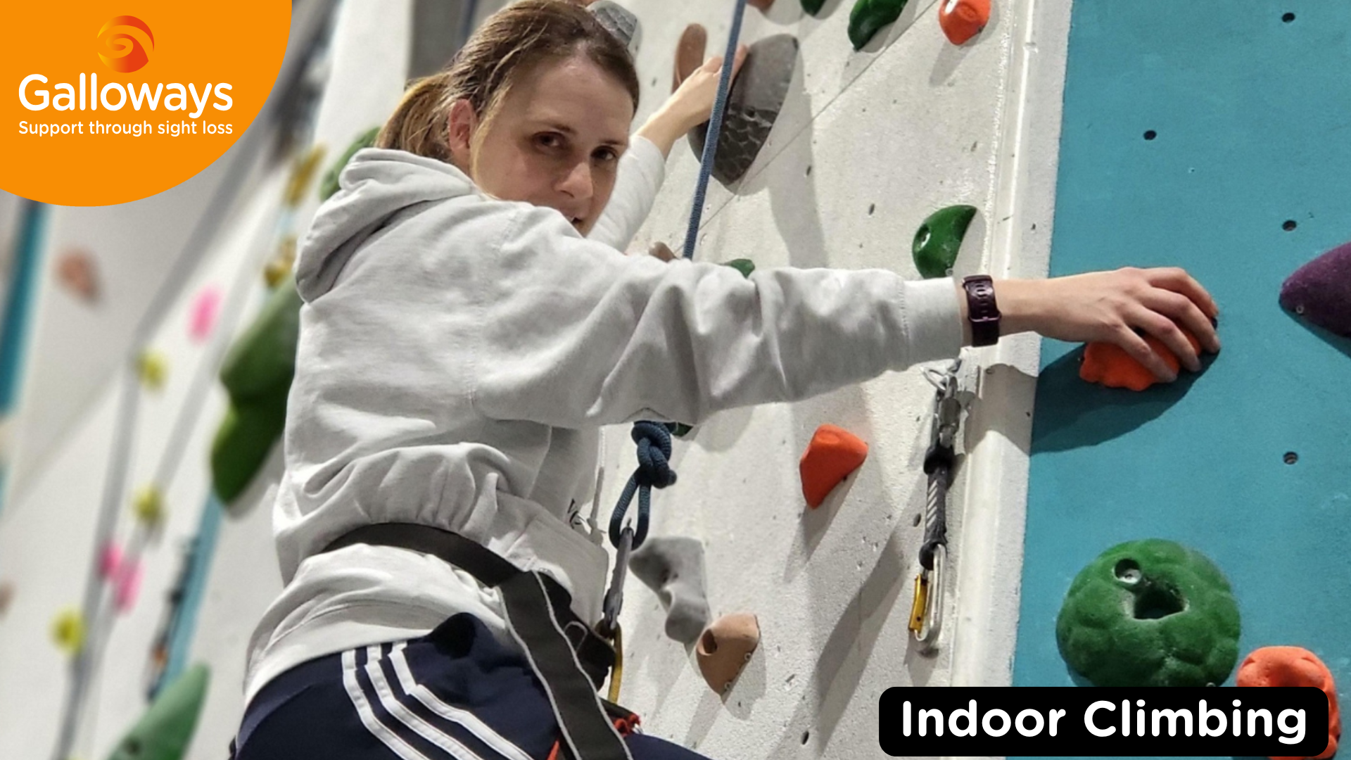A service user climbing on a wall with a harness around them. The Galloways logo is in the top left corner on top of a orange semi-circle. In the bottom right corner is a caption stating, " indoor climbing".