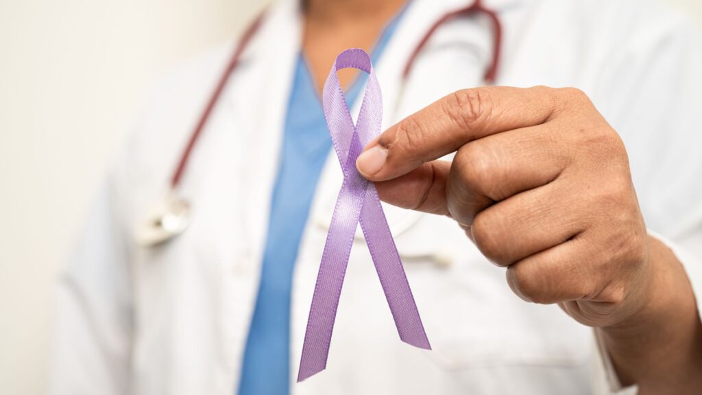 A picture depicting a doctor's coat and stethoscope in the background, with a hand holding a lilac ribbon depicting pancreatic awareness