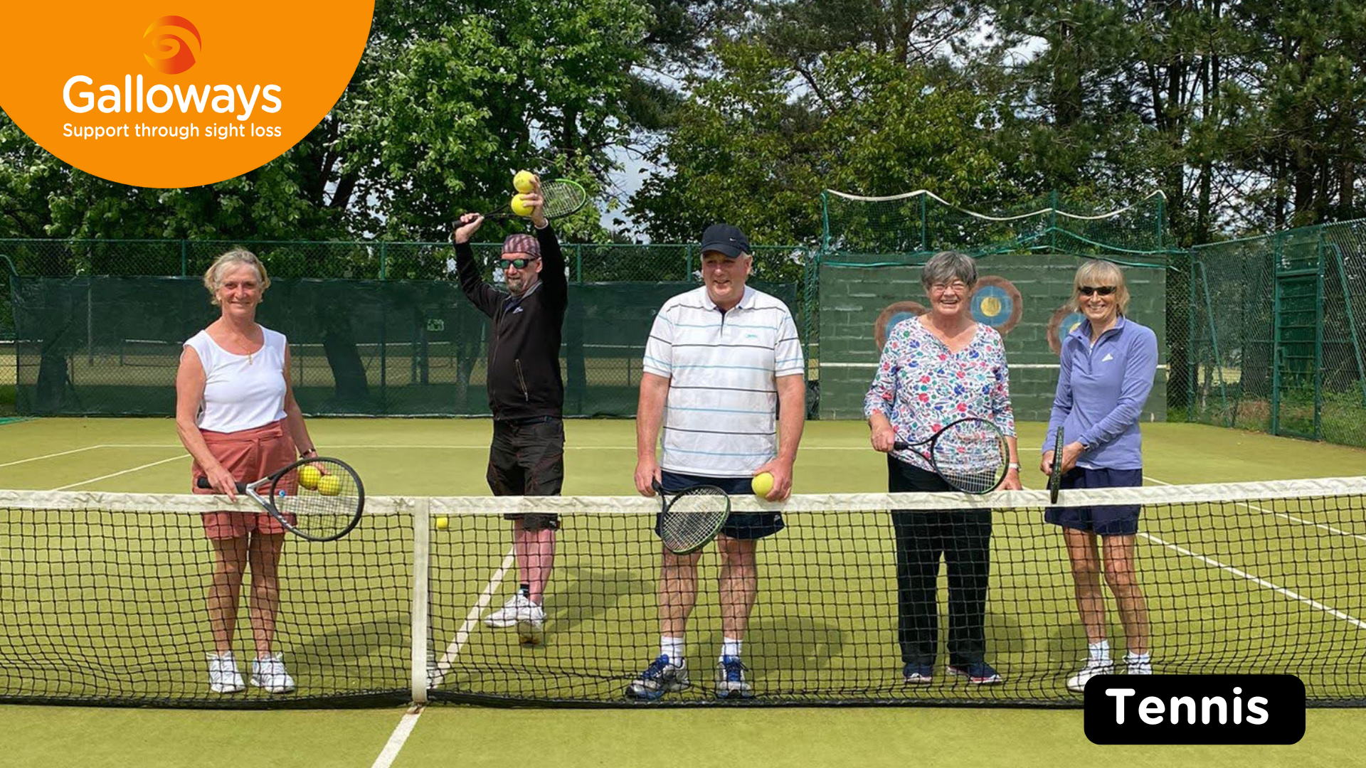 5 people on a tennis court outside, behind the net and all holding tennis rackets.