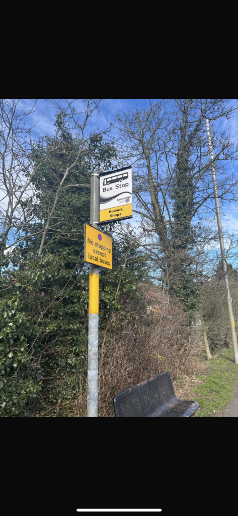 A picture of the bus stop at Howick shops next to a black bench and some trees. As the change to a Penwortham bus route will be happening the x2 bus will be stopping here.