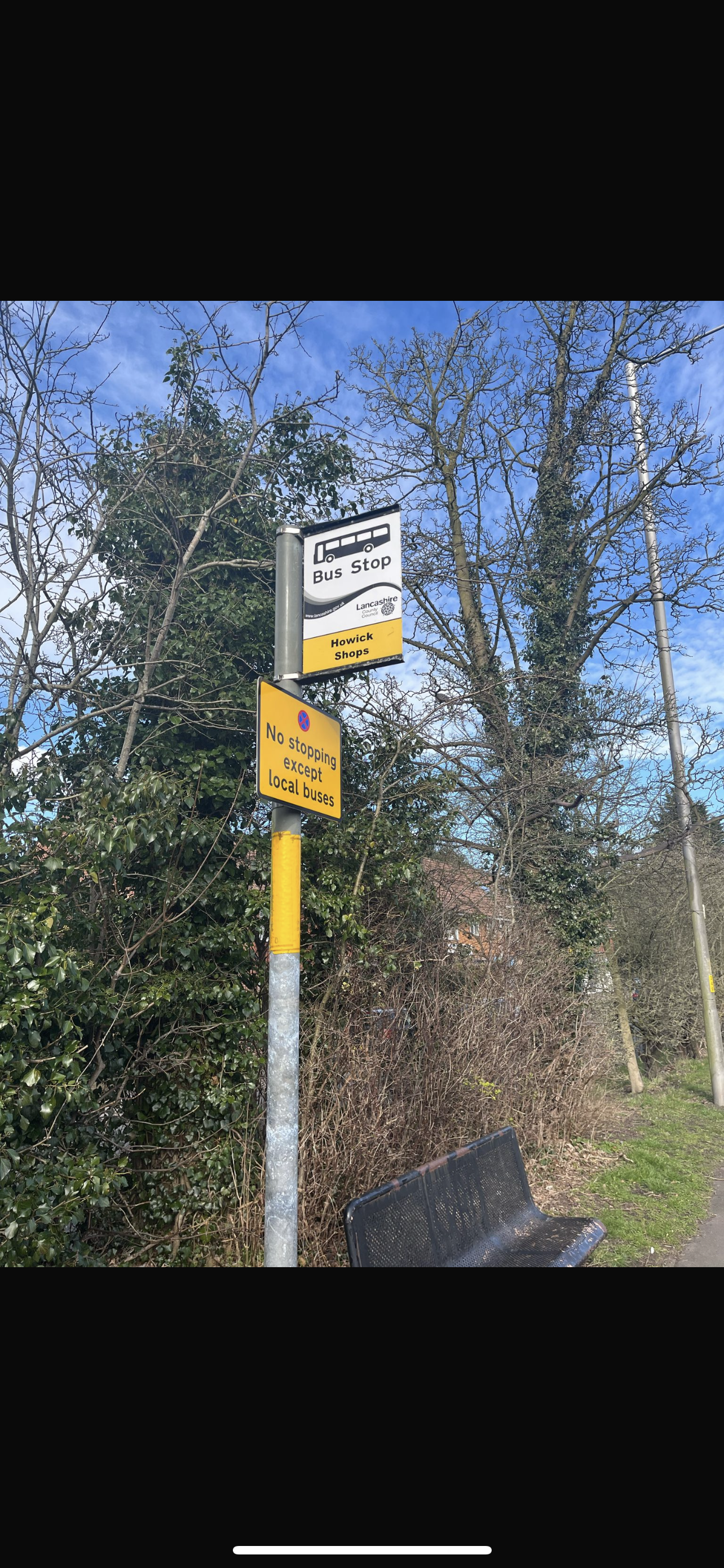 A picture of the bus stop at Howick shops next to a black bench and some trees. As the change to a Penwortham bus route will be happening the x2 bus will be stopping here.