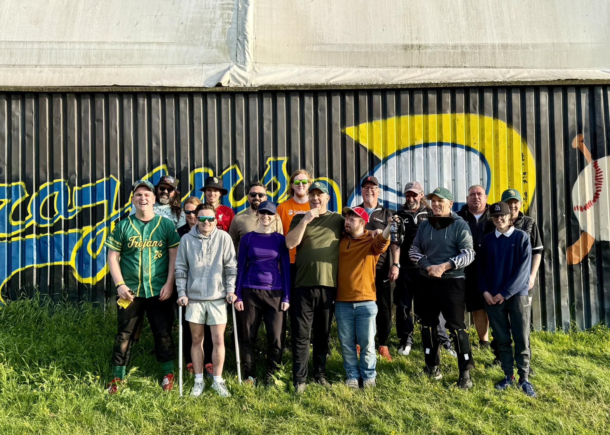 A large group of VI baseball players in front of a graffitied background all smiling at the camera