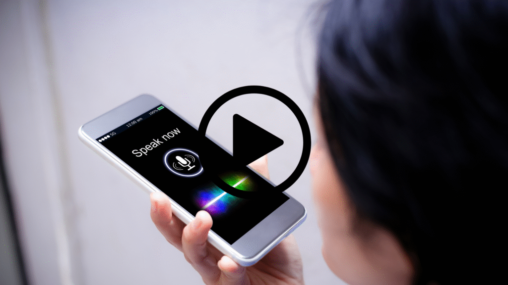 Someone holding a mobile phone to their mouth speaking into it. The screen of the phone shows a microphone icon and reads "speak now".