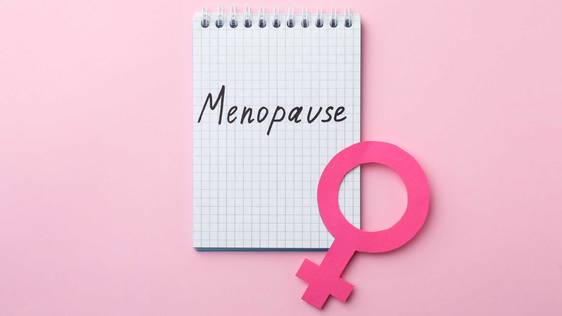 A light pink background with a white notepad in the centre with the word "menopause" written in black handwriting, with the universal symbol for female situated diagonally in the corner.