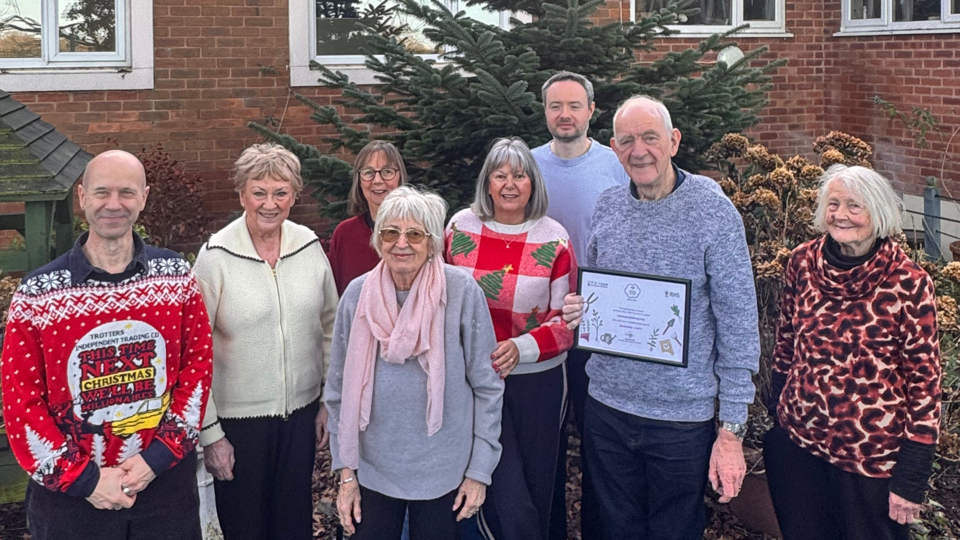 8 members of the Galloways gardening group smiling and proudly showing an award.