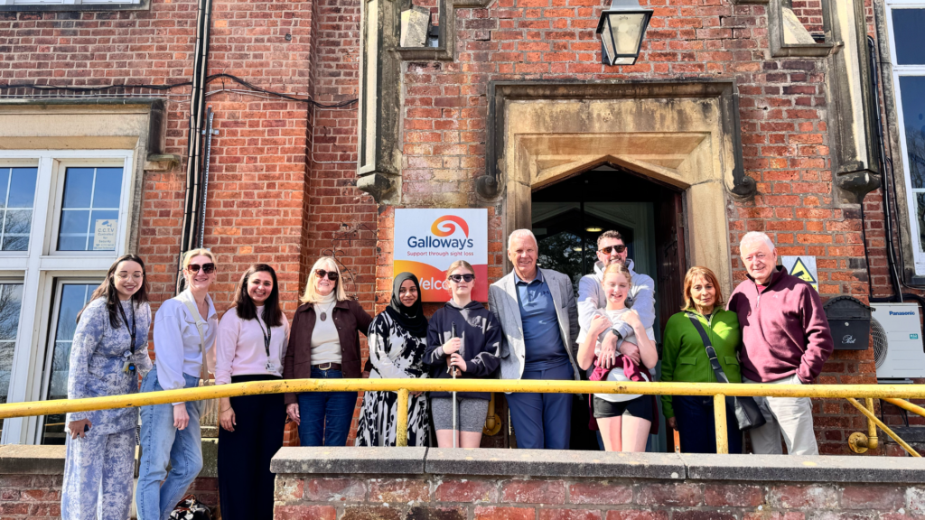 Poppy, wearing her Meta glasses, stood beside her family members, members from the golf club, and staff from Galloways outside the Galloways building on a sunny day.