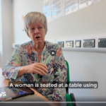 A woman demonstrates the Synapptic accessibility interface on a tablet using touch gestures and spoken feedback.