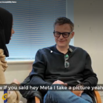 A gentleman sat in a chair wearing a pair of Meta AI glasses, in conversation with another person receiving a demonstration on using the glasses.